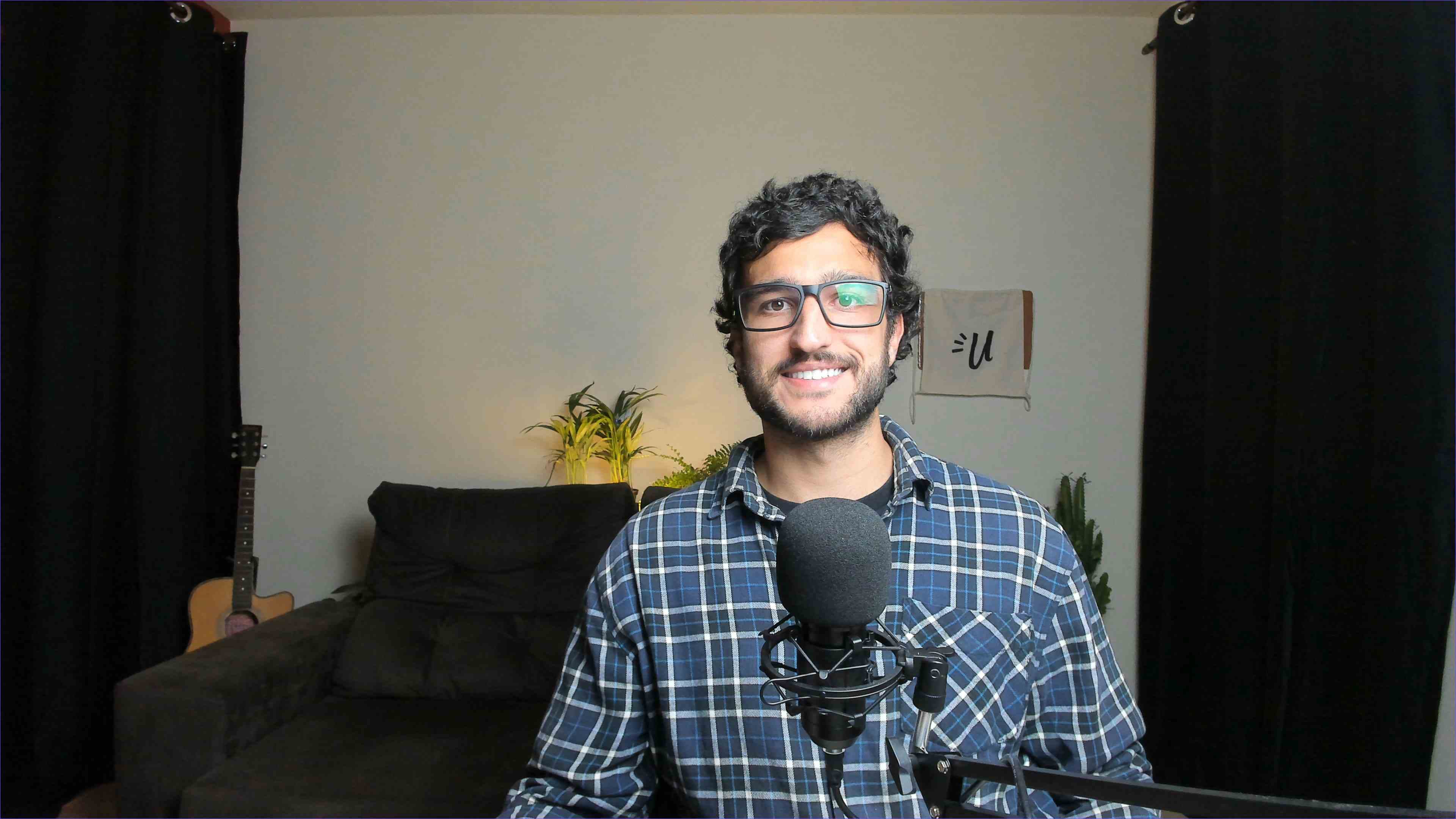 Thomas in front of a podcast microphone in his home studio, with an acoustic guitar in the background.